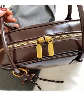 Detail of a brown leather bag showing dual gold zippers and sleek woven drawstring side