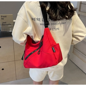 Detail of red nylon tote bag featuring adjustable black shoulder strap and zipper