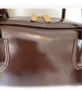 Detail of dark brown glossy tote bag showing gold logo and fine stitching texture