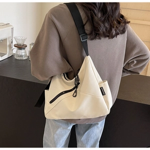 Detail view of large beige crossbody tote bag with side logo tag and wide black strap