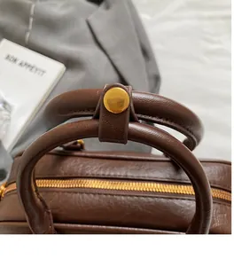 Detail of brown leather handbag featuring dual cylindrical handles and gold zipper closure