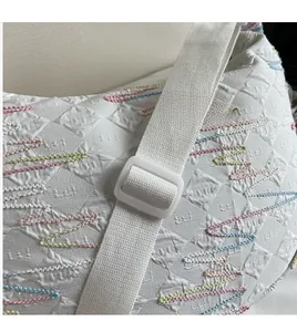 Close-up of embroidered wavy pattern and adjustable woven strap on white fabric crossbody bag