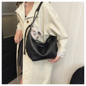 Detail showing high-quality black leather hobo bag with a plush rabbit charm and knotted strap