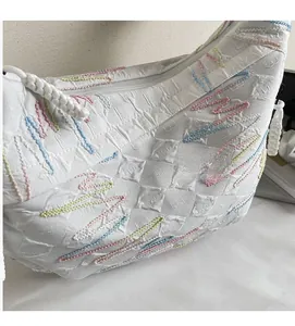 Detail of white pleated shoulder bag featuring colorful wavy embroidery and quilted texture