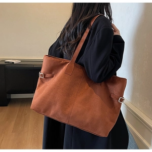 Detail of caramel suede tote bag with adjustable metal buckles on a black coat model