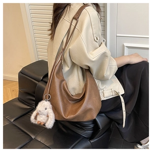 Close-up of a large brown leather tote bag with a white plush bunny charm on a model