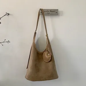 Detail of tan suede Hobo shoulder bag with round pendant and visible stitching