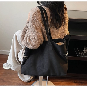 Detail of large black suede tote bag with adjustable metal buckle on shoulder strap