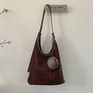 Detail of dark brown matte suede bucket bag with round charm and detachable strap
