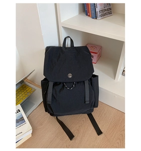 Détail d'un sac à dos en nylon noir avec logo métallique sur un sol en bois clair d'intérieur