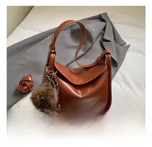 Détail du sac en cuir marron avec finition cirée, bandoulière large et pompon en fourrure