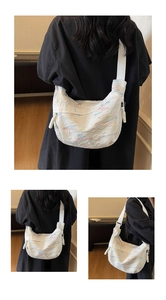 Detail of white half-moon crossbody bag featuring colorful embroidery and woven strap