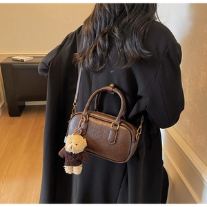 Detail of a brown Boston bag with leather texture and a cute bear charm for women