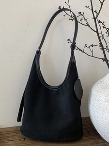 Matte black suede hobo shoulder bag with round charm shown in a minimalist interior setting