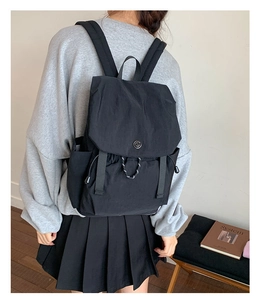 Detail of black nylon backpack featuring flap closure and drawstring on model