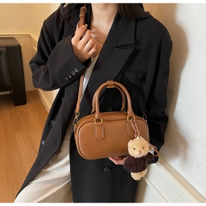 Detail of brown leather Boston bag featuring Mira Mira embossed logo and plush bear charm