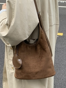 Minimalist dark brown suede bucket bag with round charm shown in outdoor scene