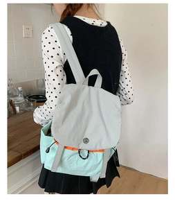 Close-up of the light gray flap and mint green canvas backpack worn by a model