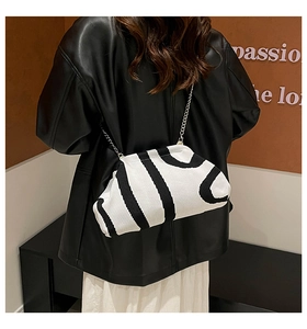 Detail of knitted cloud bag with bold black stripes and a silver chain strap on a model
