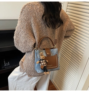Detail of blue denim bucket bag with leather pocket, metal rivets and a cute bunny charm