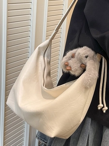Chic beige crescent tote bag with plush bunny charm shown on a stylish shoulder strap