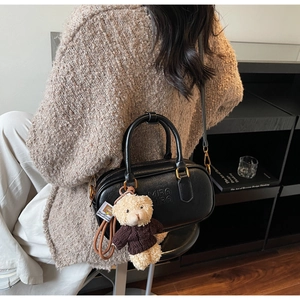Detail of black leather crossbody bag with embossed logo and a brown teddy bear charm