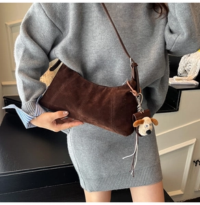 Detail view of brown vintage crescent shoulder bag with a cute dog plush charm accessory
