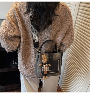 Detail of grey matte bucket bag with geometric strap and plush rabbit charm