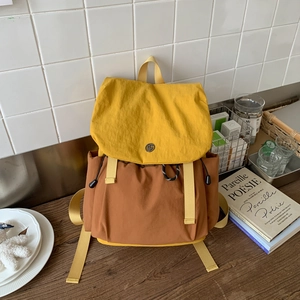 Detail view of the yellow flap and metal logo buckle on the color-block canvas backpack