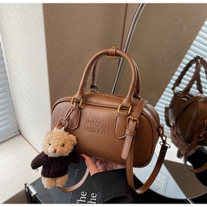 Detailed view of dark brown textured PU leather Boston bag with Mira Mira logo and bear charm