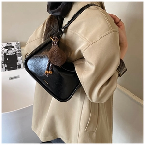 Vue détaillée du sac à bandoulière noir brillant avec logo doré et breloque en peluche