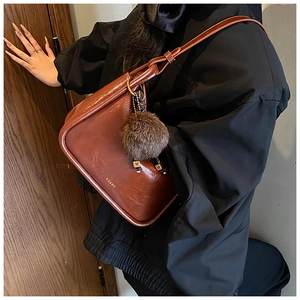 Détail du sac rétro en cuir marron avec logo doré et accessoire de boule en peluche