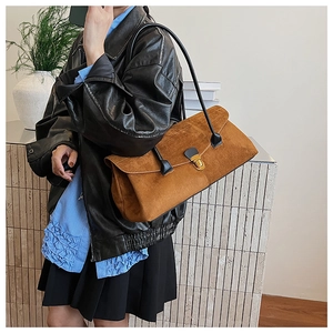 Detail of a brown suede shoulder bag with a gold clasp being worn in a minimalist setting