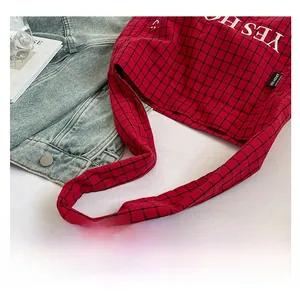 Detail der rot-schwarz karierten Canvas-Tasche mit weißem Text und breitem Schultergurt