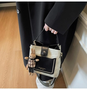 Detail of color-block bucket bag with metal rivets, logo text and cute rabbit pendant