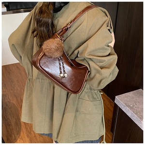 Détail du sac bandoulière marron brillant avec pompon en peluche et logo AM gravé