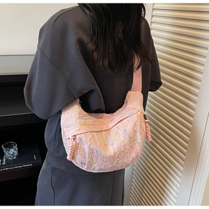 Pink quilted crescent crossbody bag with embroidery detail and wide woven strap on model