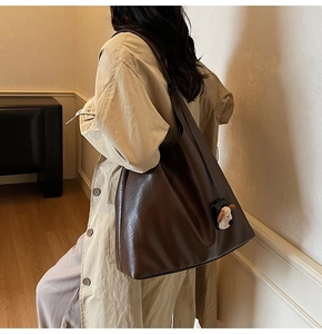 Detail view of a large dark brown leather tote bag with a cute plush dog charm