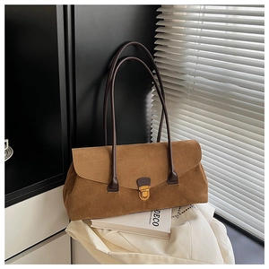Close-up of brown suede underarm bag with gold metal buckle on white deco art books