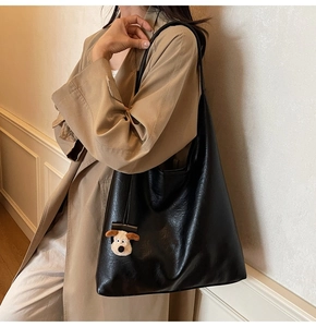 Detail of a black large-capacity tote bag with a plush dog charm on a model in a trench coat