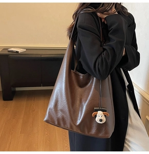 Detail showing the brown vintage leather tote bag with a white plush puppy charm