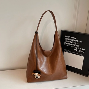Detail view of brown matte leather hobo bag with a cute plush dog pendant on white surface