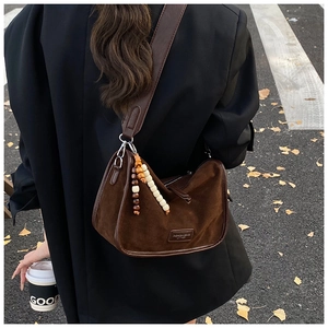 Detail einer braunen Wildleder-Hobo-Tasche mit Perlenanhänger und breitem Schultergurt