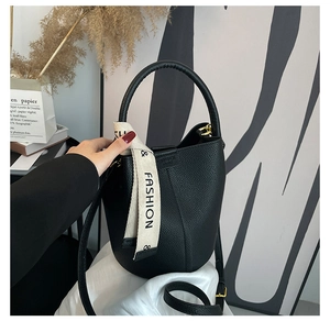 Detail view of black lychee grain leather bucket bag with a stylish logo canvas strap