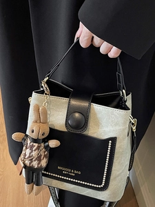Fashionable bicolor bucket bag in cream woven fabric and black leather with plush charm