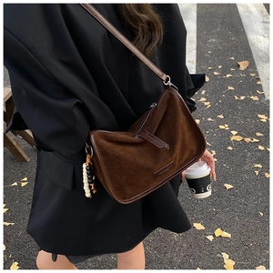 Detailansicht einer braunen Wildlederhandtasche mit Perlenanhänger in herbstlicher Umgebung