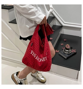 Detail einer rot-schwarz karierten Canvas-Tasche mit weißer Stickerei auf einer Treppe
