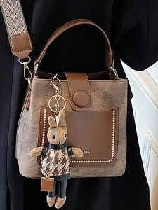 Vintage brown bucket bag with wide strap and rabbit charm, autumn 2025 fashion style