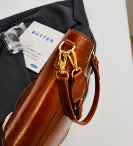 Close-up of golden hardware hooks and polished brown oil-wax leather texture on bucket bag