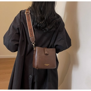 Détail d'un sac seau en cuir marron foncé avec large bandoulière brodée élégante